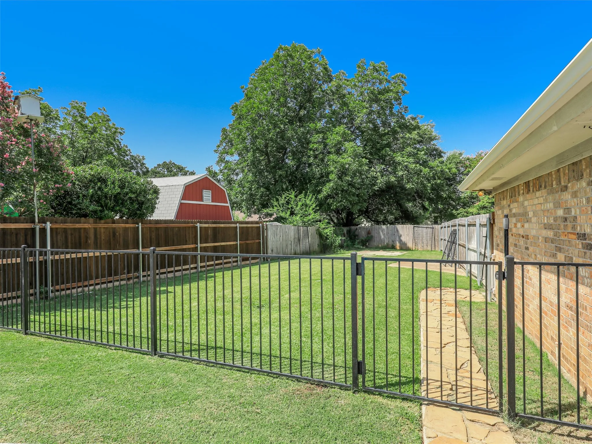 Expansive backyard featuring a lush lawn, black metal fencing, and a stone pathway