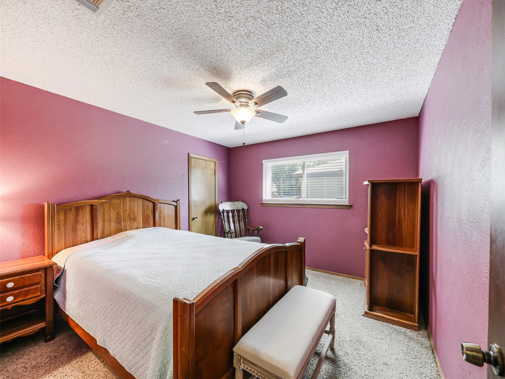 Bedroom featuring wood-finish door, window with blinds, ceiling fan, and textured ceiling