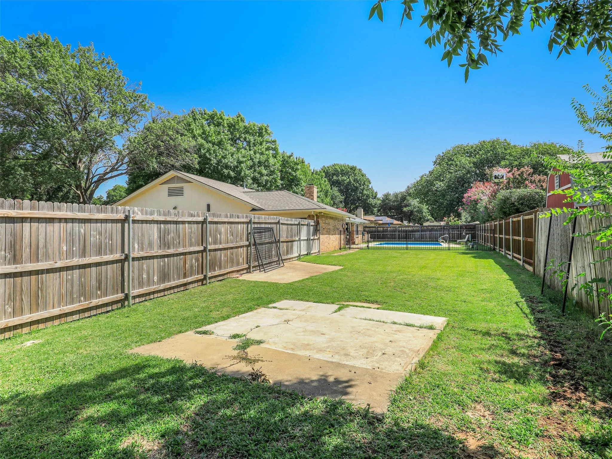 Expansive backyard featuring a rectangular swimming pool, concrete patio, mature trees, and privacy fencing
