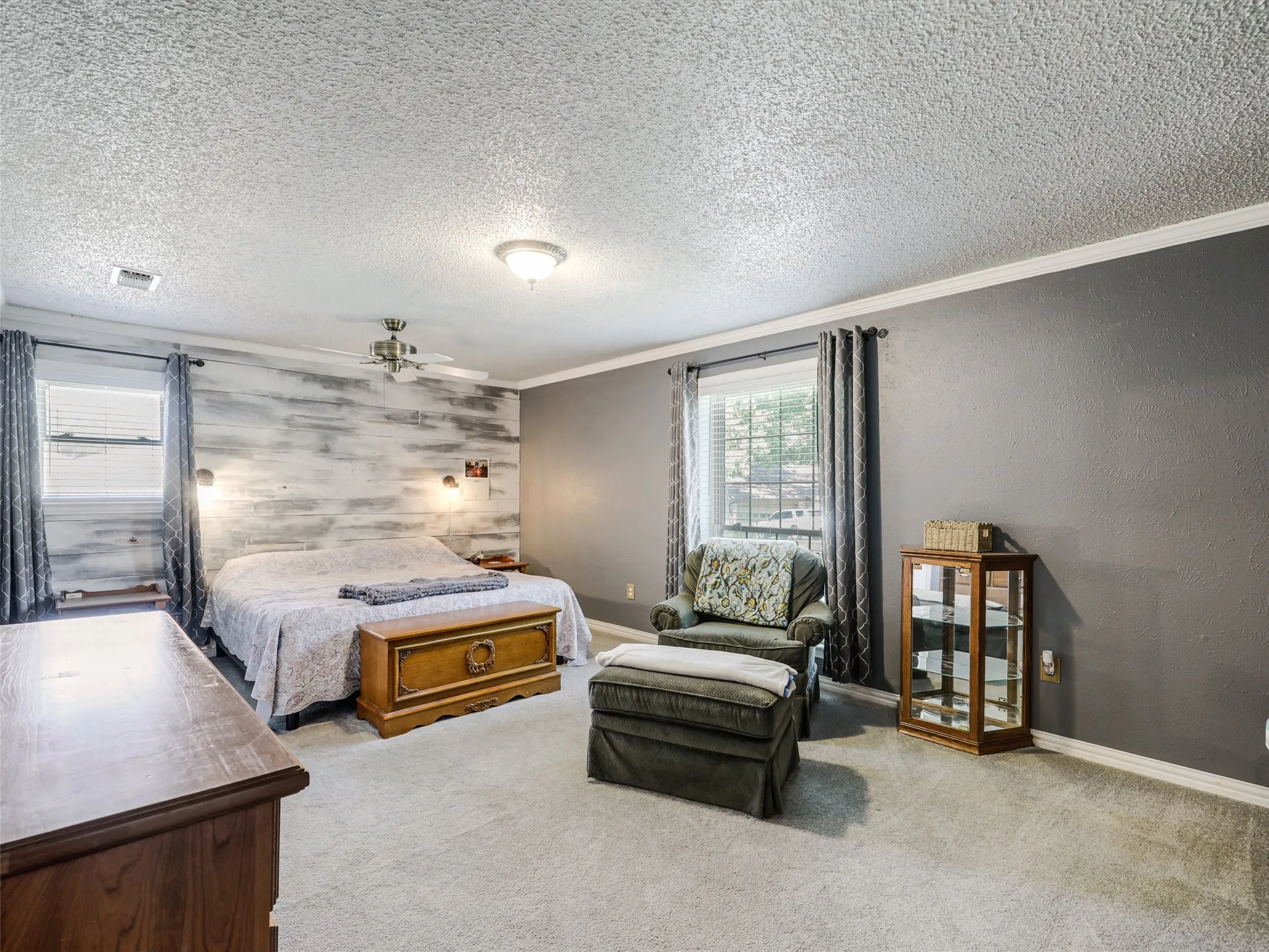 Spacious bedroom featuring a textured accent wall, light grey carpeting, recessed lighting, and a ceiling fan