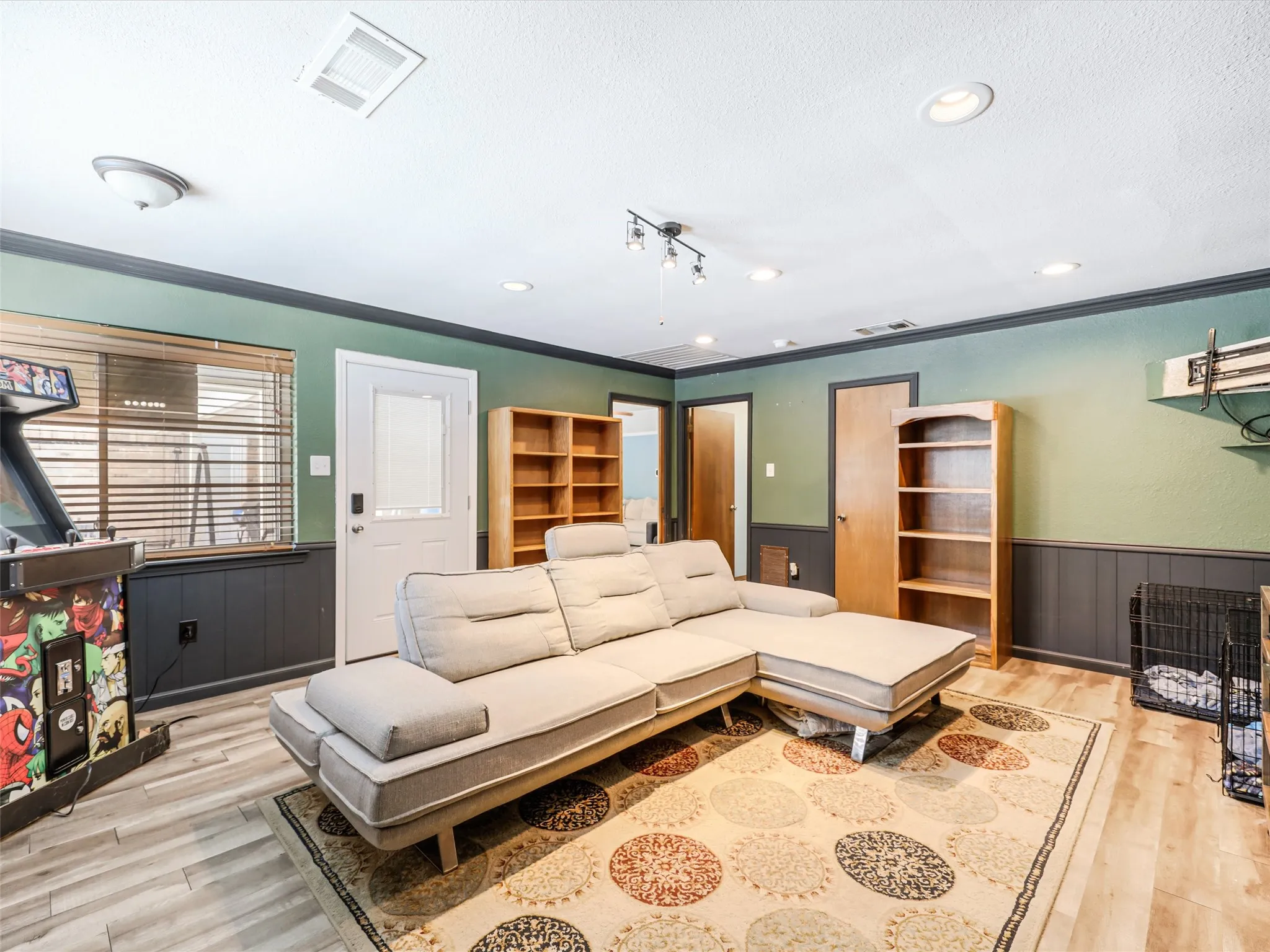 Spacious room with wood-finish flooring, two-tone wall paint, a white door, and multiple lighting fixtures