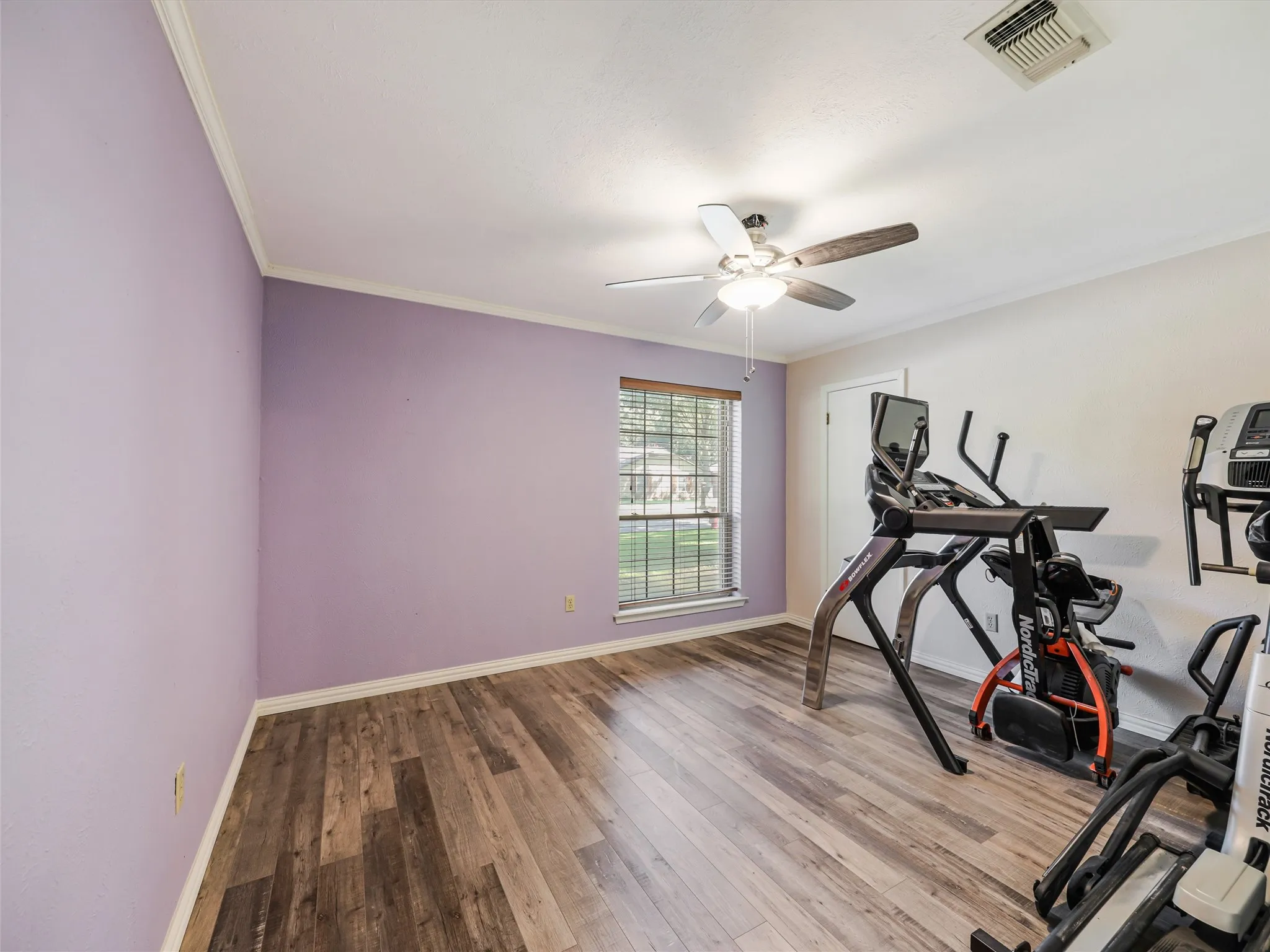 Spacious room featuring wood-finish flooring, a ceiling fan with integrated lighting, and a window with blinds