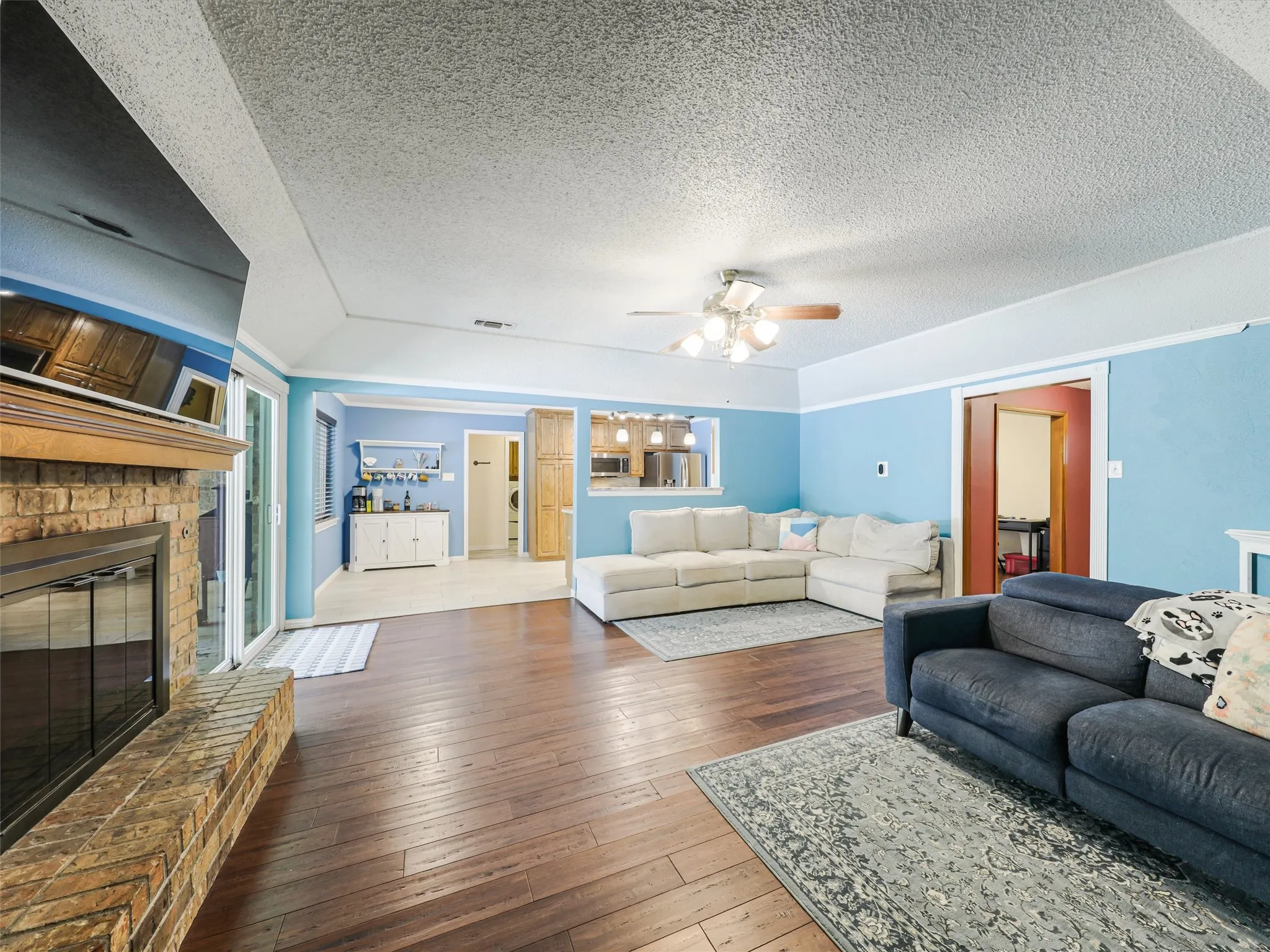 Spacious living area featuring wood-finish flooring, a brick-surround fireplace with a wood mantle, and an integrated ceiling fan