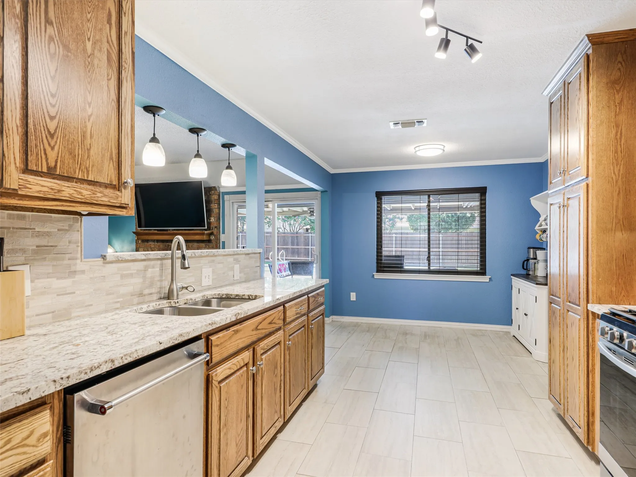 Kitchen featuring wood cabinetry, light-toned countertops, a stainless steel double basin sink with a gooseneck faucet, and a stainless steel dishwasher