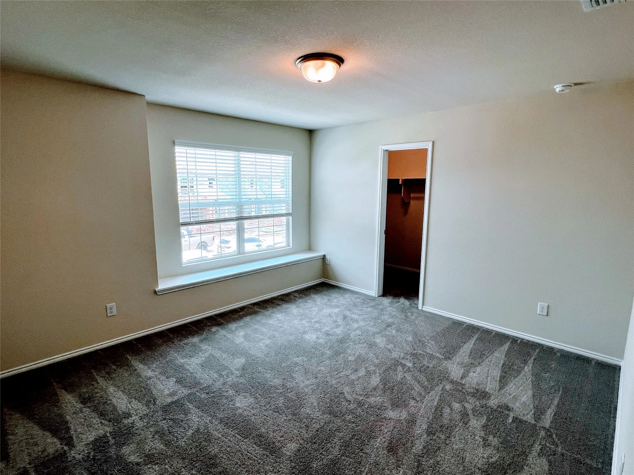 Carpeted room with a large window featuring blinds and a deep sill