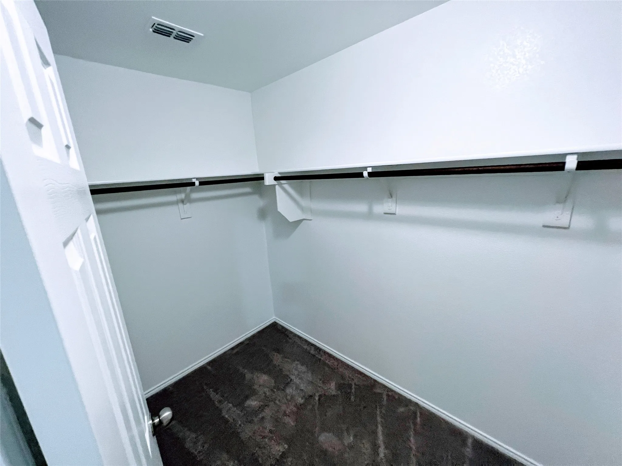 Walk-in closet featuring a neutral color palette, integrated hanging rods, and dark-toned flooring