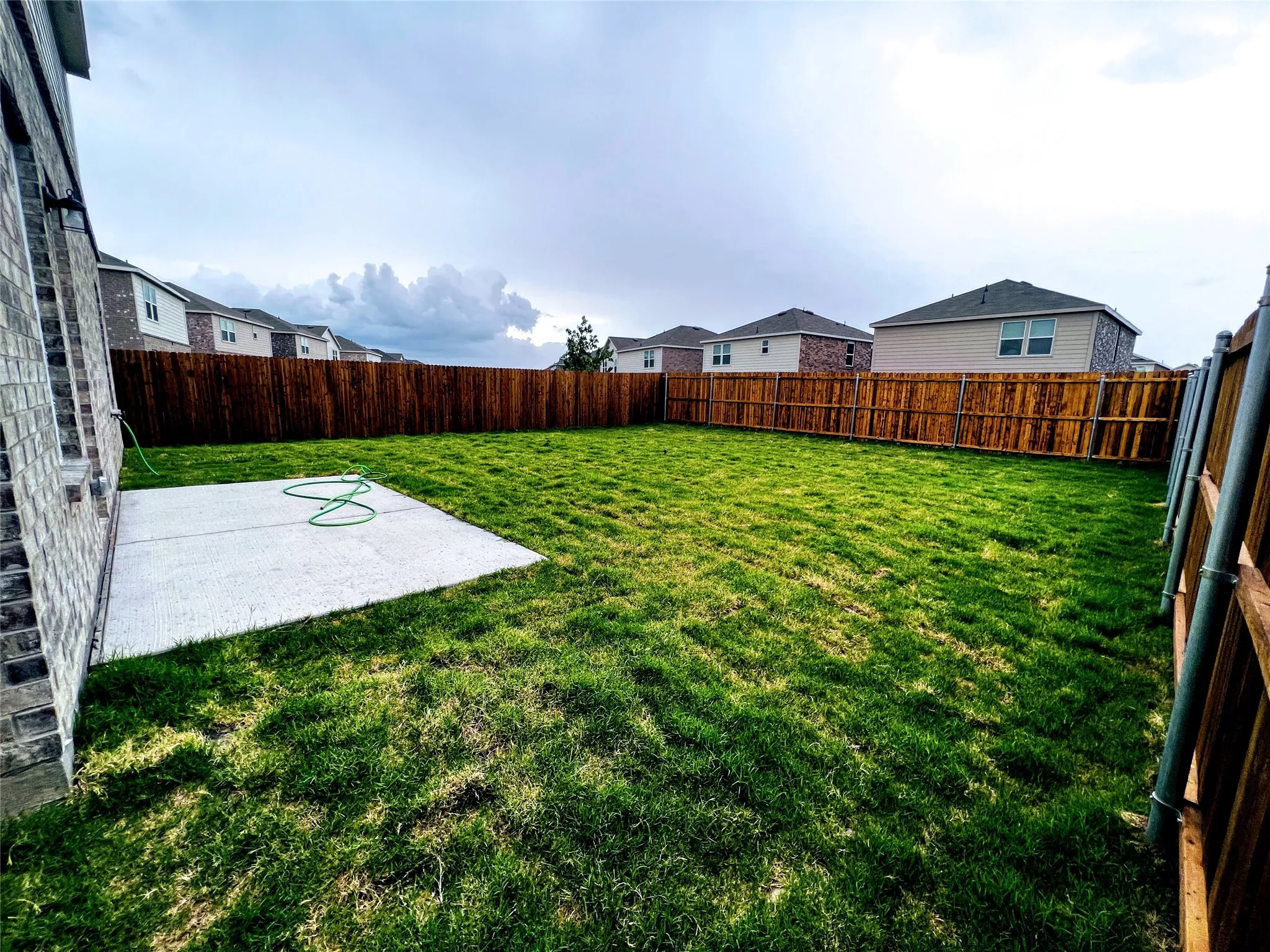 Expansive green lawn with a concrete patio, bordered by a privacy fence