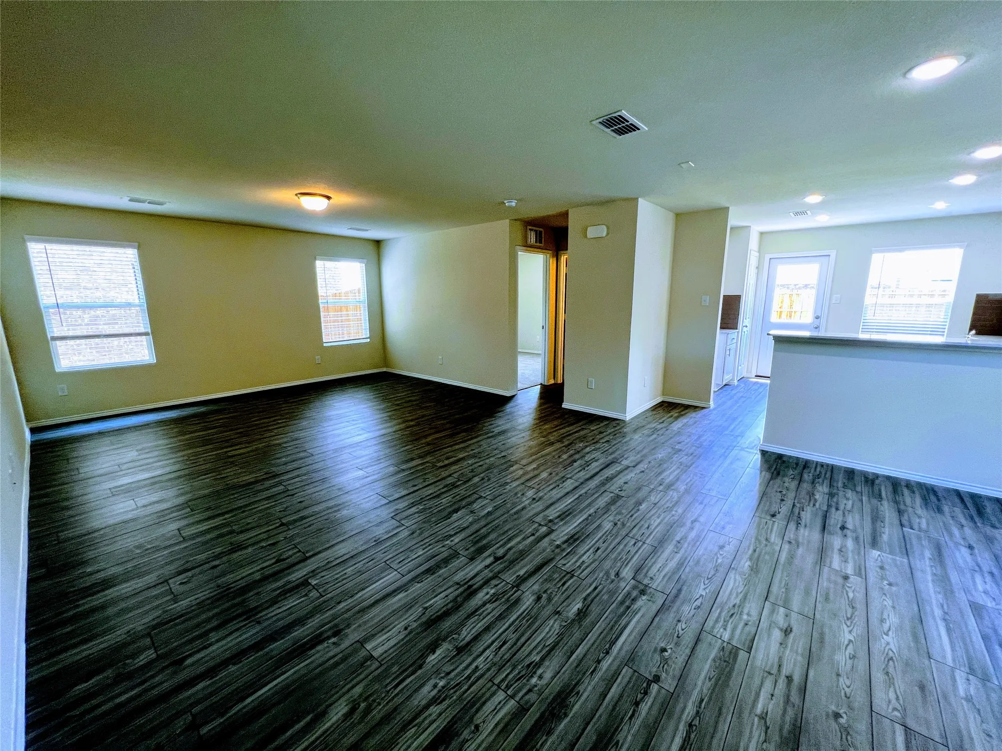 Spacious interior featuring wood-finish flooring, neutral-toned walls, multiple windows with blinds, recessed lighting, and a prominent half-wall divider