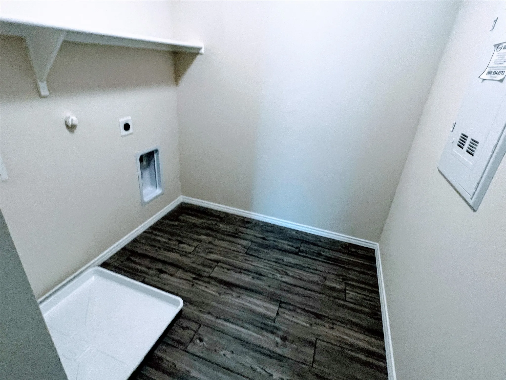 Dedicated utility space featuring wood-finish flooring, white baseboards, and a wall-mounted shelf