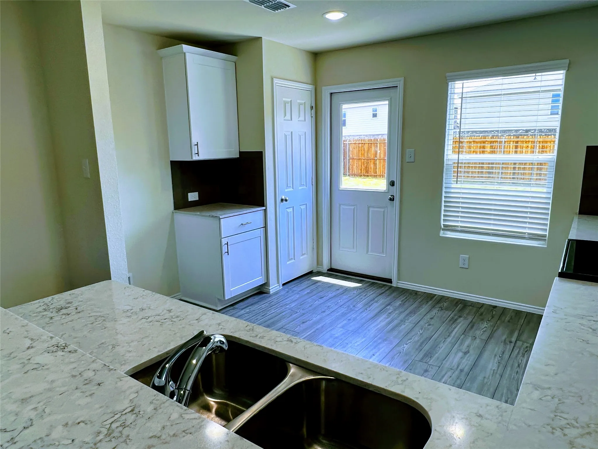 Kitchen featuring quartz countertops, a dual basin stainless steel sink, white cabinetry with contemporary hardware, wood-finish flooring, and a rear exterior door with a window
