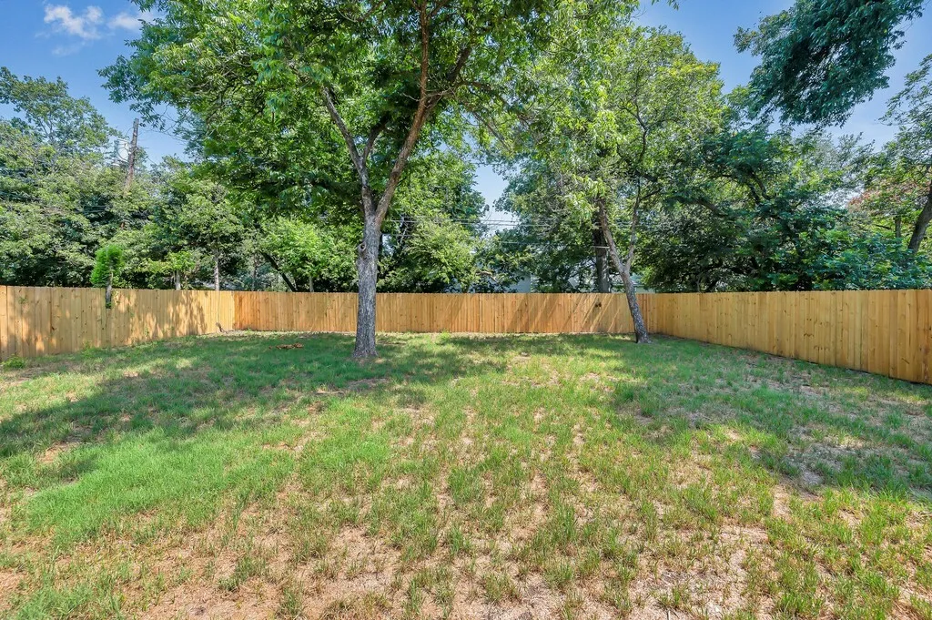 Expansive backyard featuring a natural grass lawn, mature trees providing shade, and a newly installed privacy fence