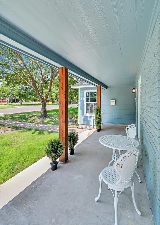 Covered front porch featuring a concrete surface, exposed wood structural columns, and a light blue painted ceiling