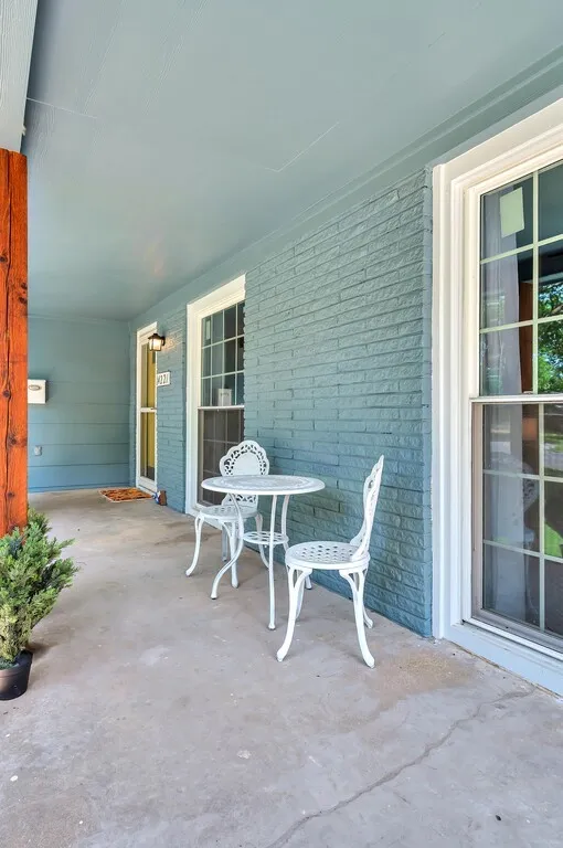 Covered concrete porch featuring a brick exterior wall, a wood support beam, and multiple windows with white trim