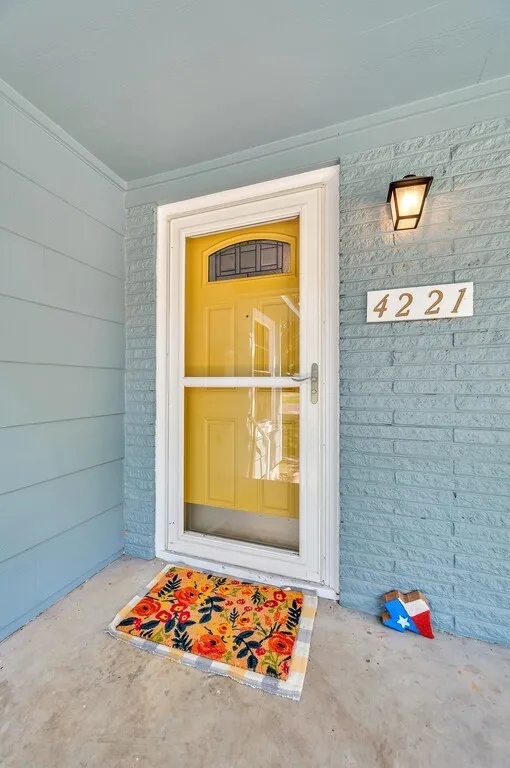 Bright yellow entry door with a storm door, sheltered by a covered porch
