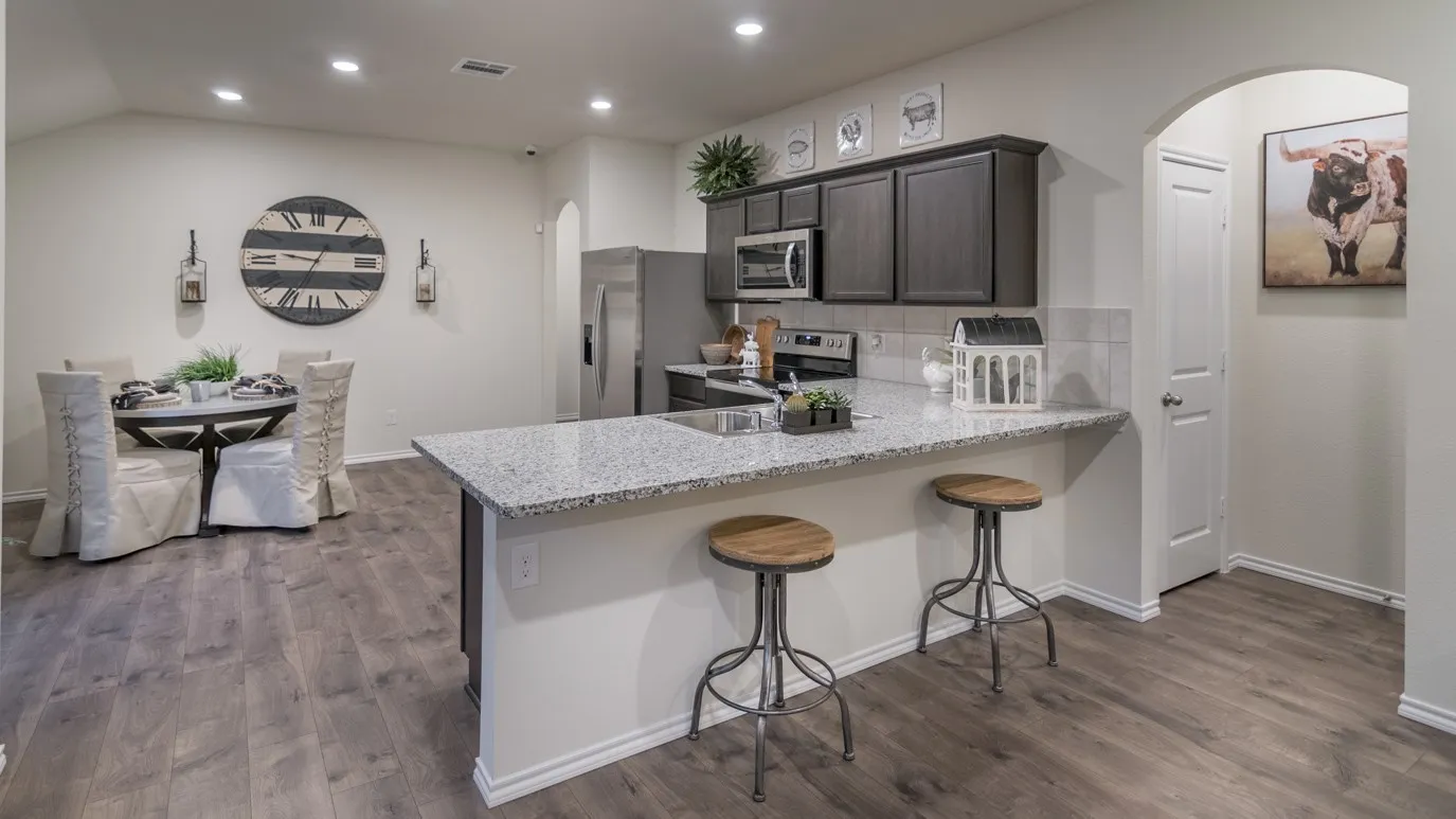 Open-concept interior featuring wood-finish flooring, a kitchen island with stone countertops and a breakfast bar, and dark wood cabinetry with stainless steel appliances