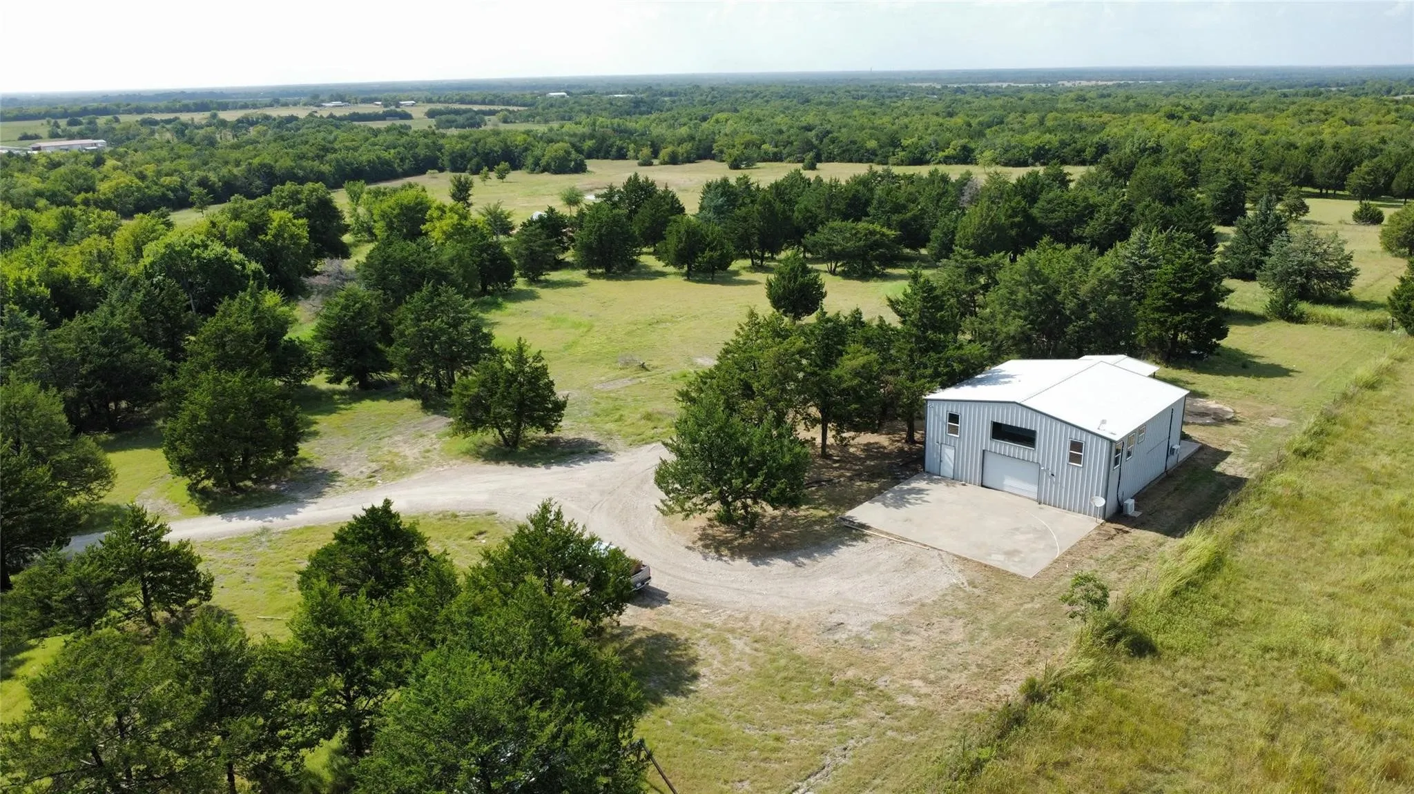 Expansive rural property featuring a large metal building with a roll-up door, a gravel driveway, and a concrete pad