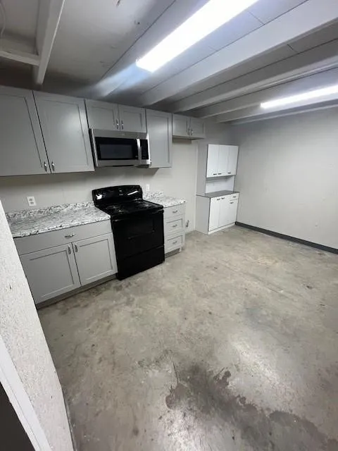 Kitchen space featuring light gray cabinetry, a black range, stainless steel microwave, and speckled countertops