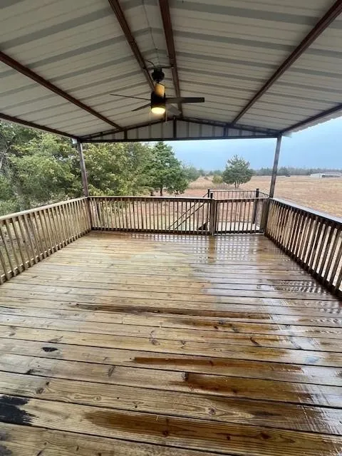 Expansive covered wooden deck featuring a metal roof structure with exposed beams, a ceiling fan with integrated lighting, and wooden railings