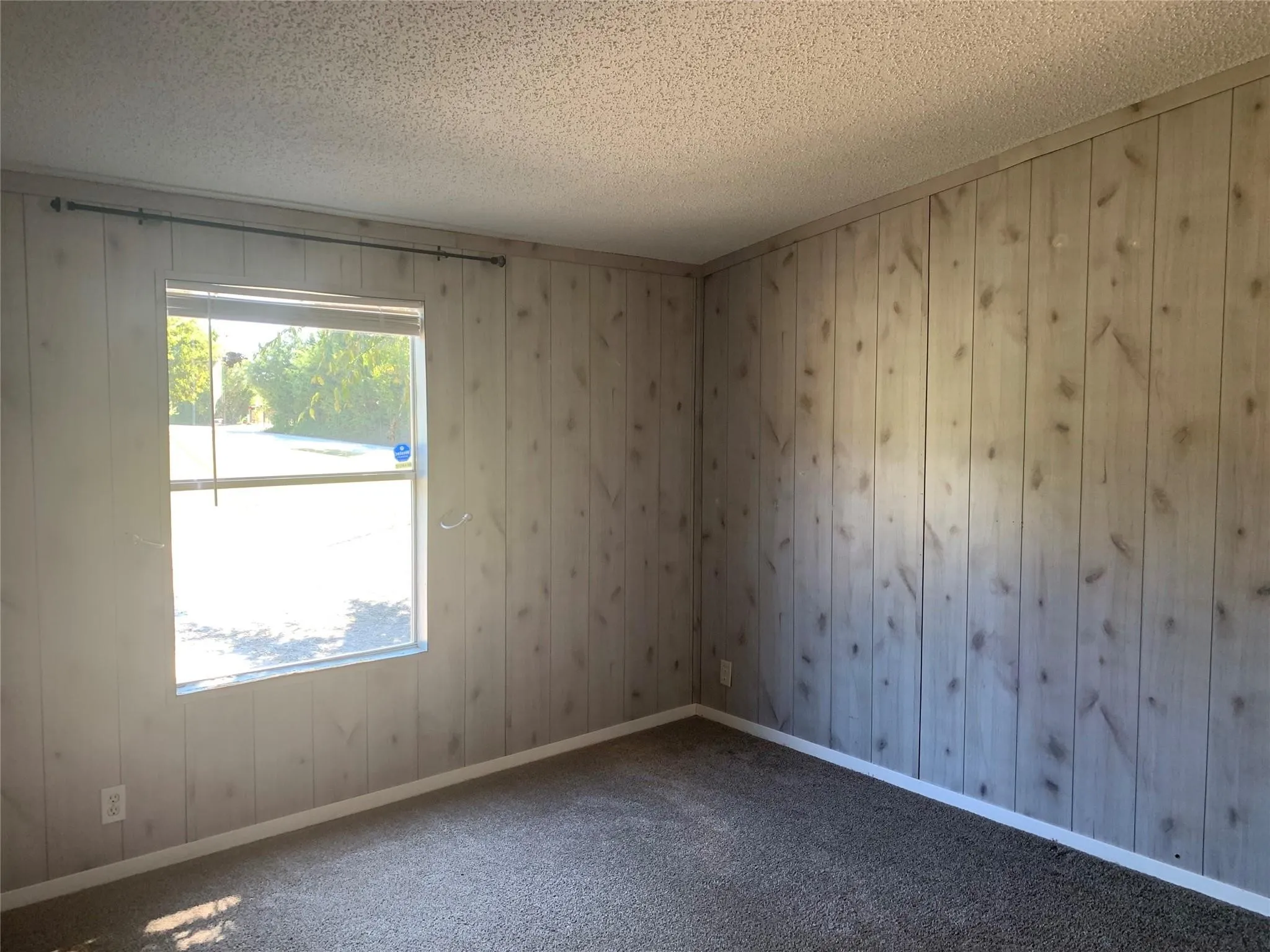 Bedroom featuring light-toned wood-paneled walls, a single pane window, dark carpet flooring, and white baseboards