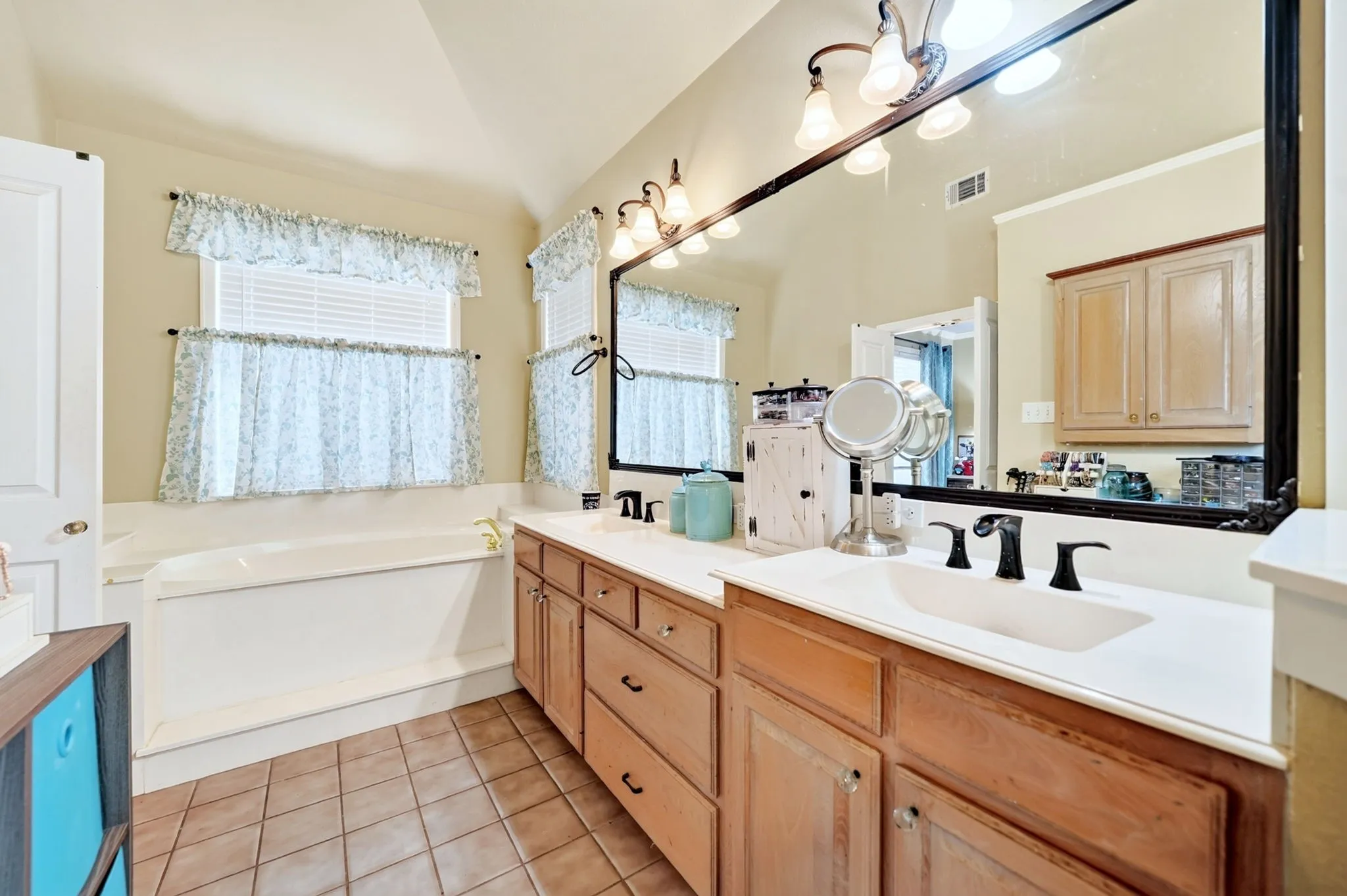 Bathroom featuring a built-in soaking tub, dual vanity with wood-finish cabinetry, and a large wall-mounted mirror