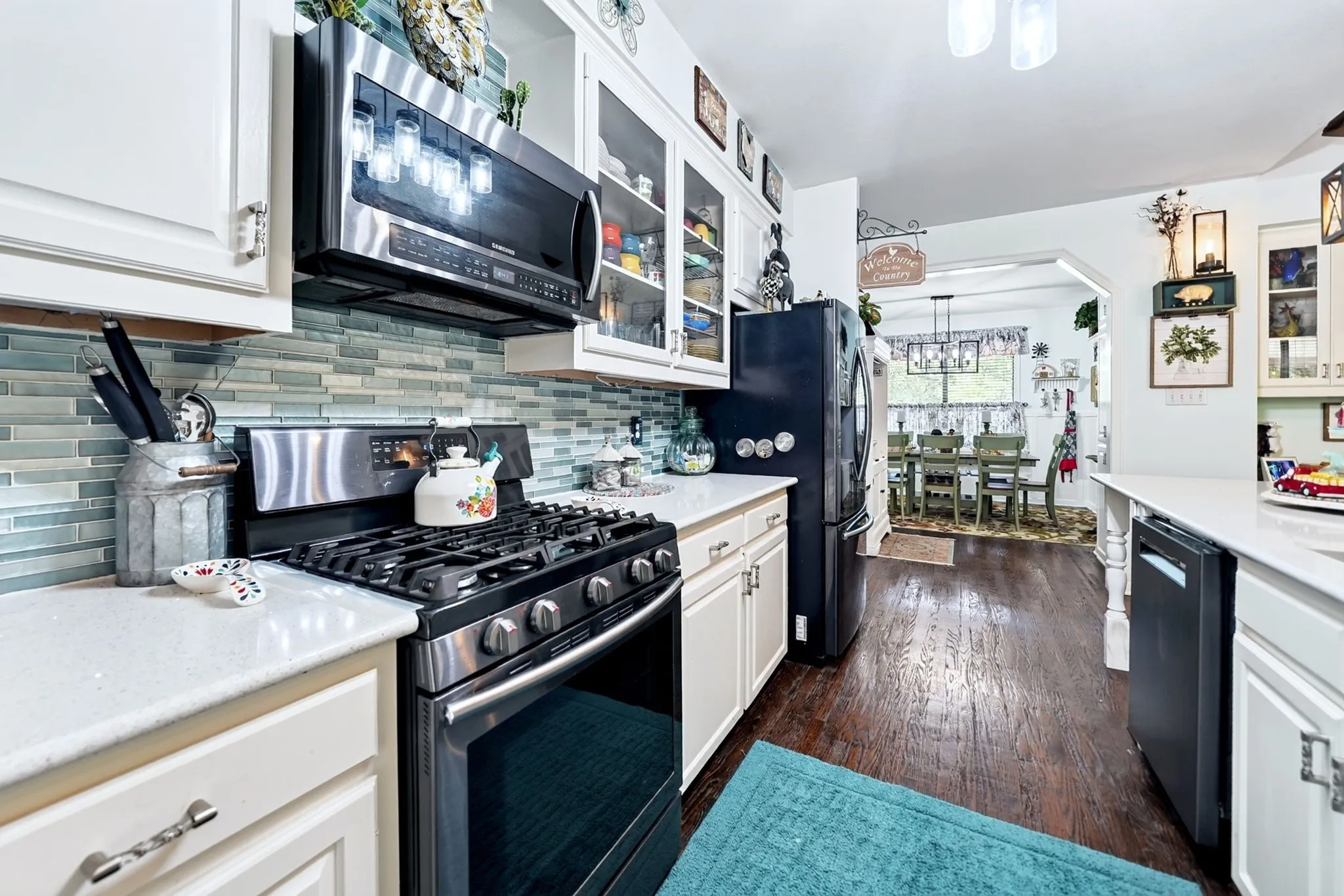 Kitchen featuring stainless steel appliances, white cabinetry with glass inserts, a tile backsplash, and light-colored countertops