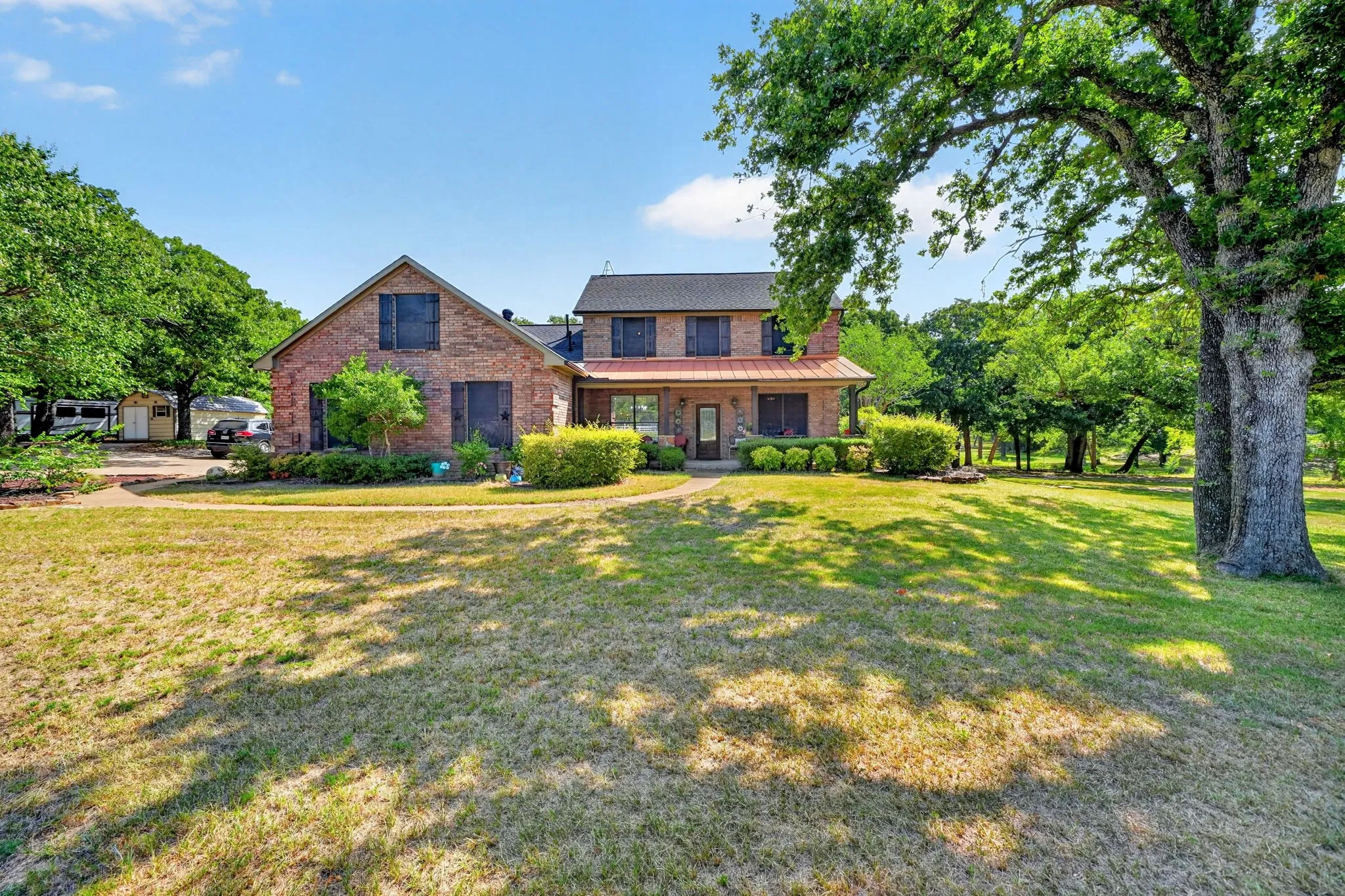 Brick exterior with copper-colored roofing accents, set amidst mature trees and a spacious lawn