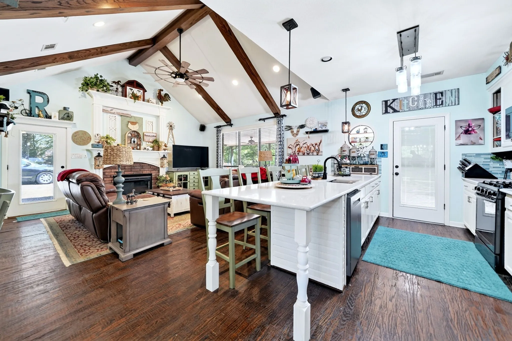 Open-concept living space featuring vaulted ceilings with exposed wood beams, dark wood-finish flooring, and a central kitchen island with a white countertop