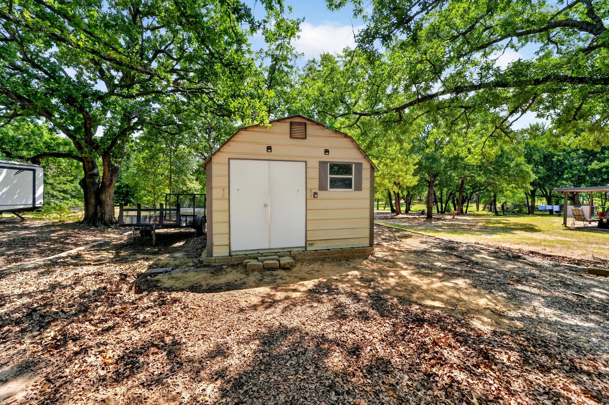 Detached storage shed with double-door entry and a single window, set on a gravel and dirt lot