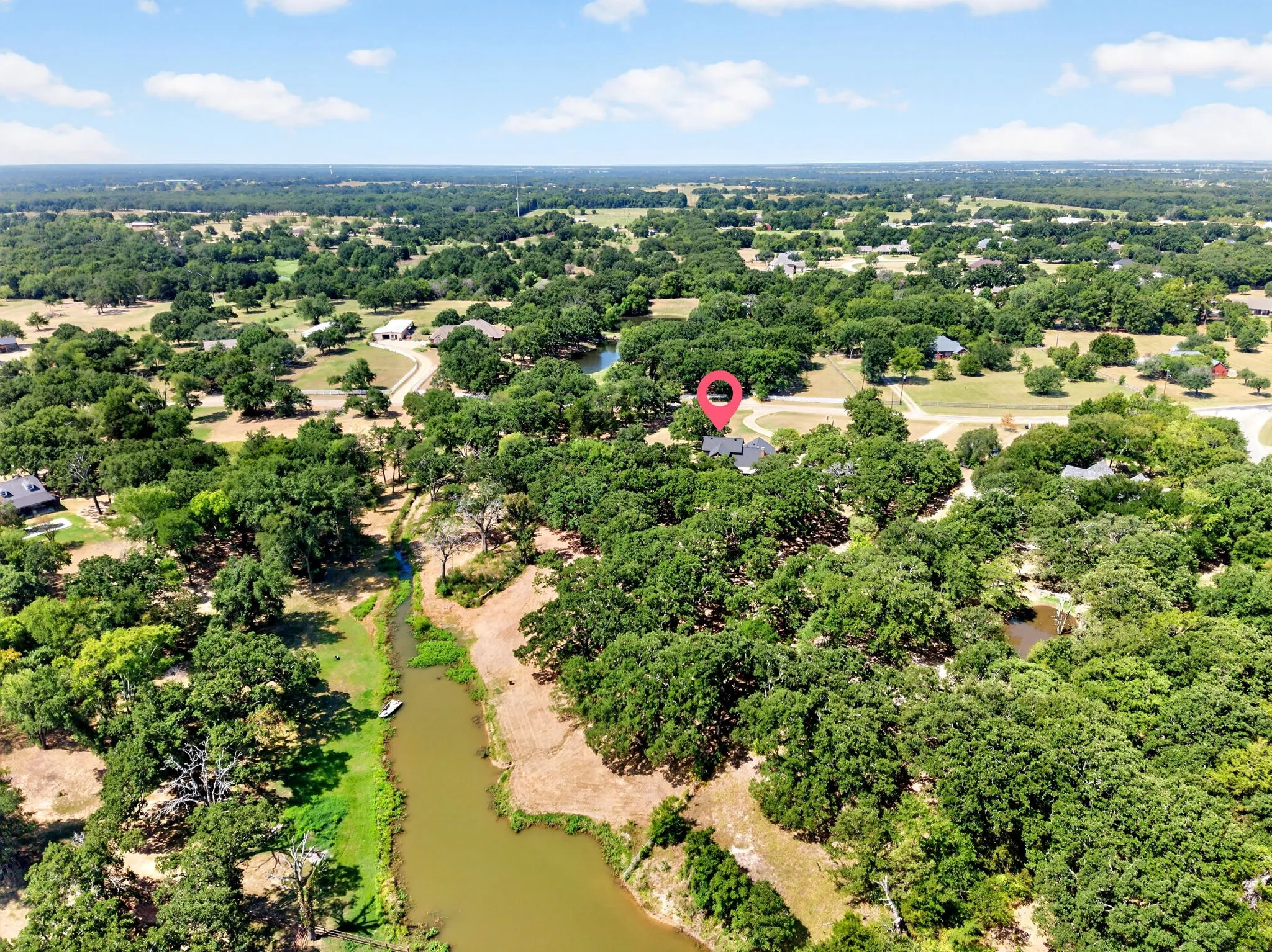 Expansive property featuring a residence nestled among mature trees, a natural water feature, and a gravel driveway