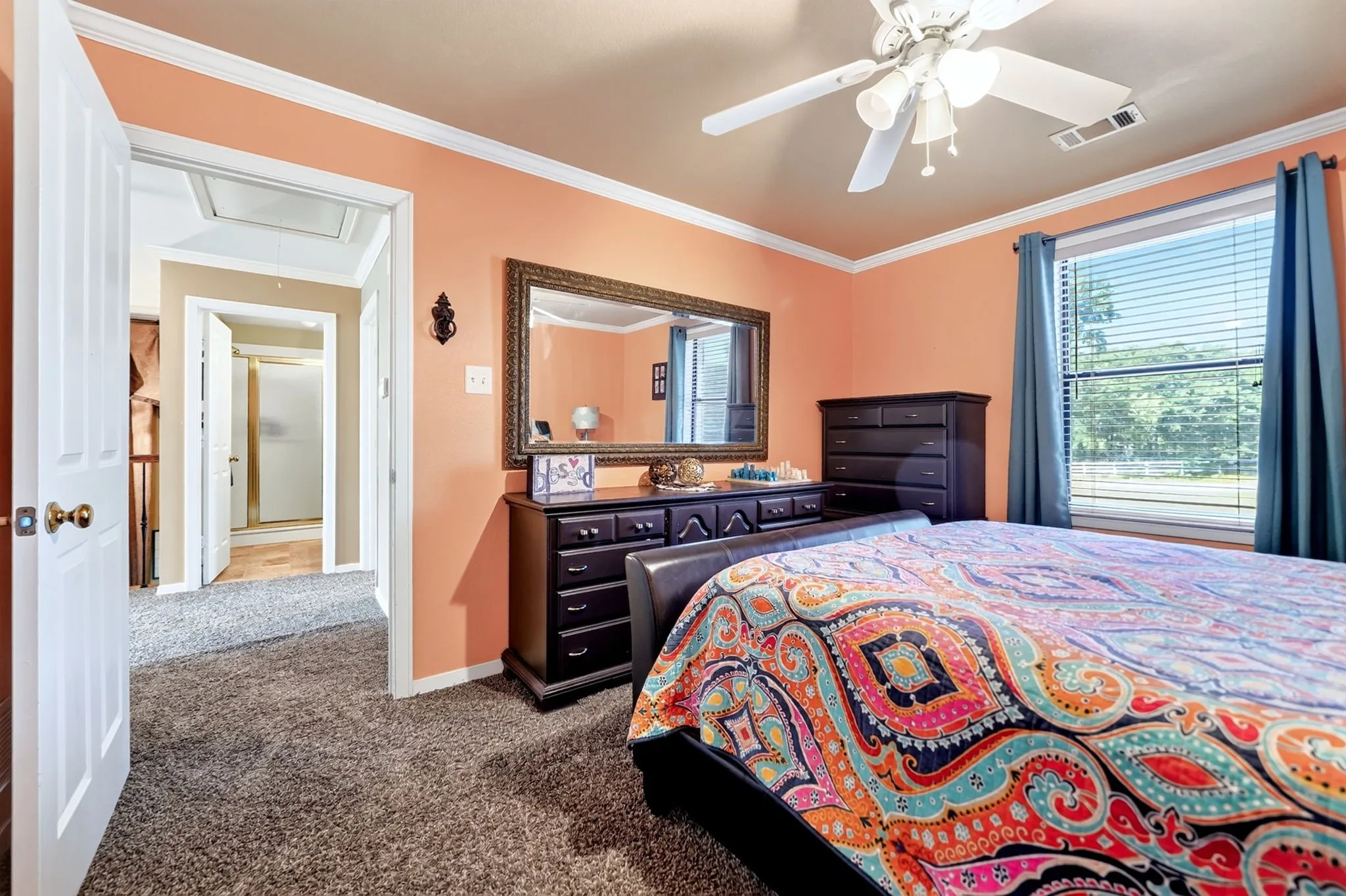 Carpeted room featuring a ceiling fan, crown molding, and a window with horizontal blinds and drapery