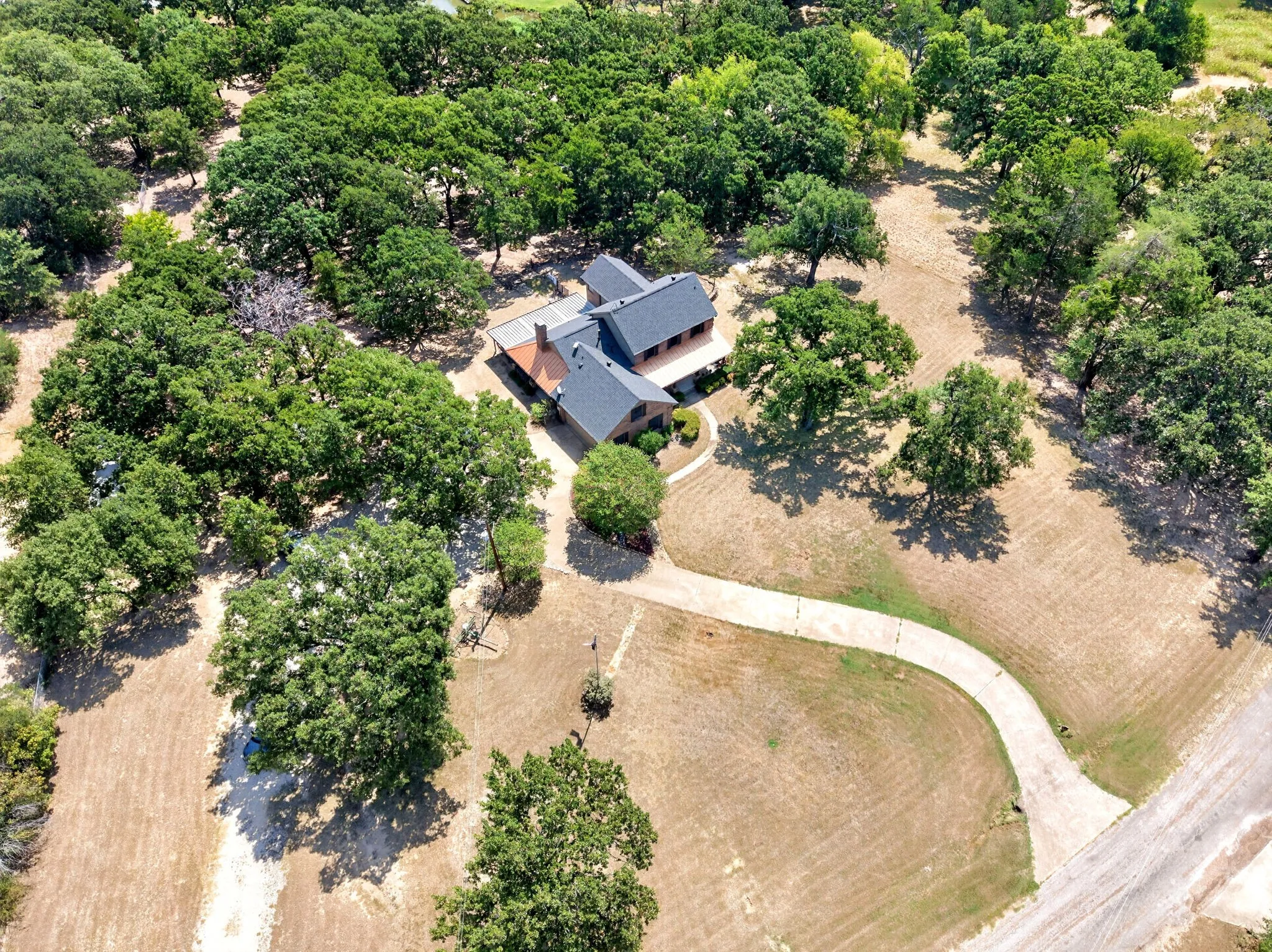 Expansive property featuring a brick home with a dark shingle roof, surrounded by numerous mature trees
