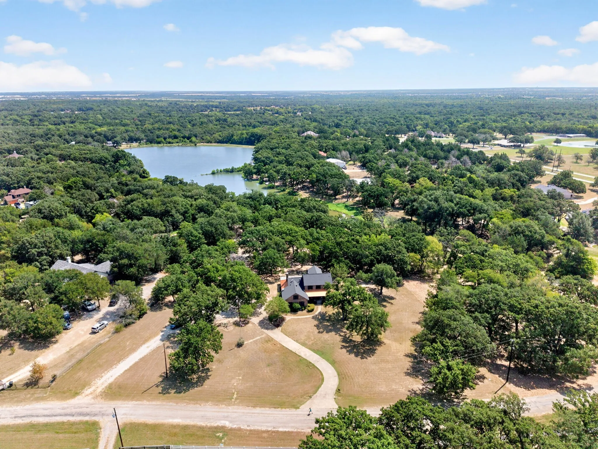 Expansive property featuring a winding driveway, mature trees, and a distant lake