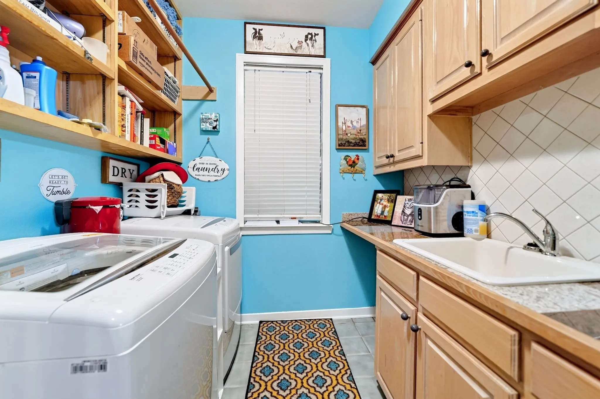 Dedicated laundry area featuring a utility sink, light wood cabinetry, and a patterned tile backsplash