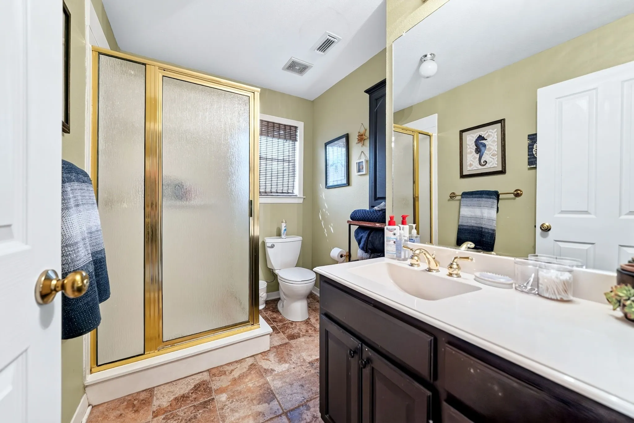 Bathroom featuring a gold-framed shower enclosure, a single vanity with a white countertop and gold-finish faucet, and tiled flooring