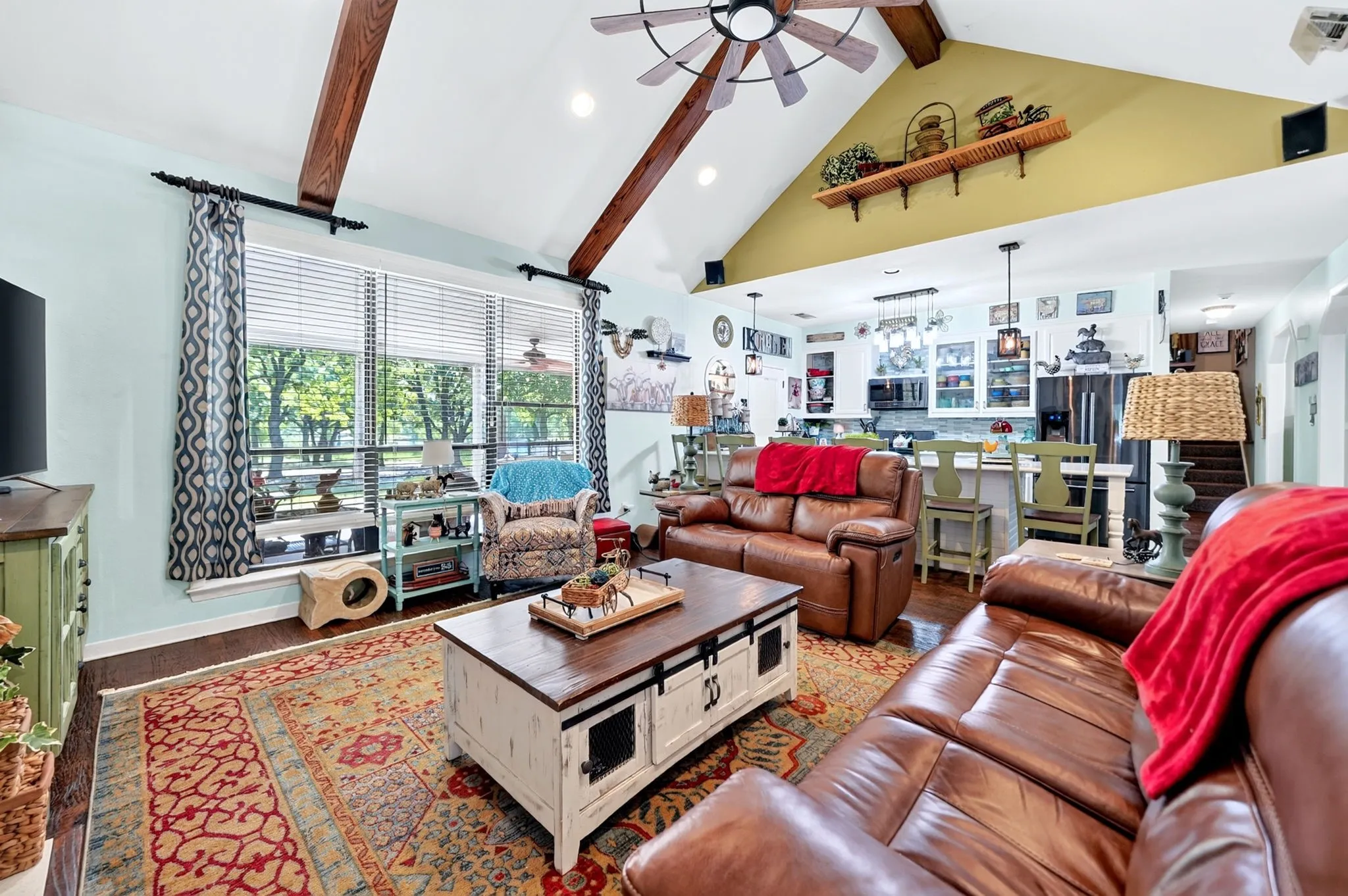 Open-concept living area featuring vaulted ceilings with exposed wood beams and a ceiling fan