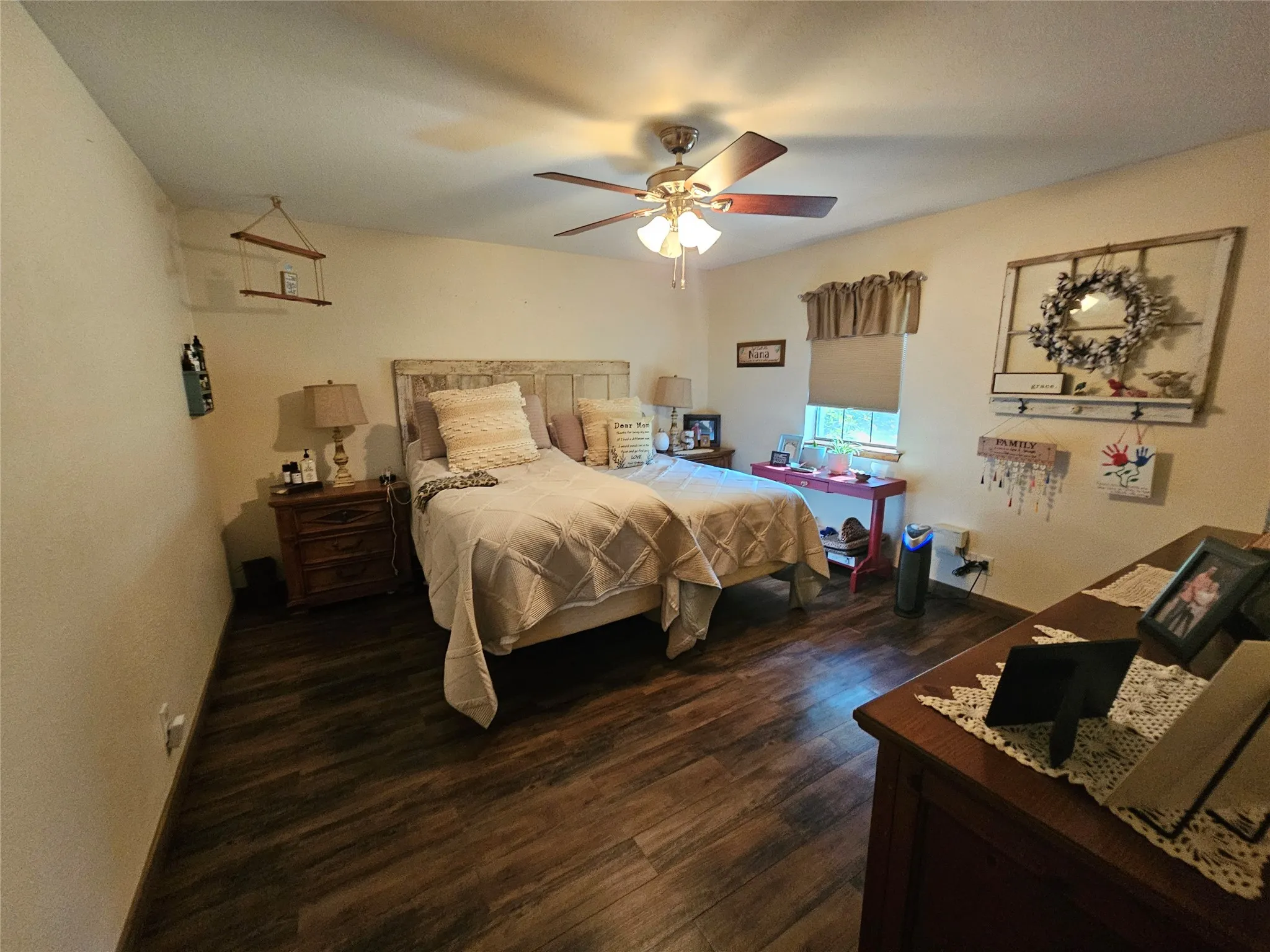 Bedroom featuring wood-finish flooring, a ceiling fan with integrated lighting, and a window with a roller shade