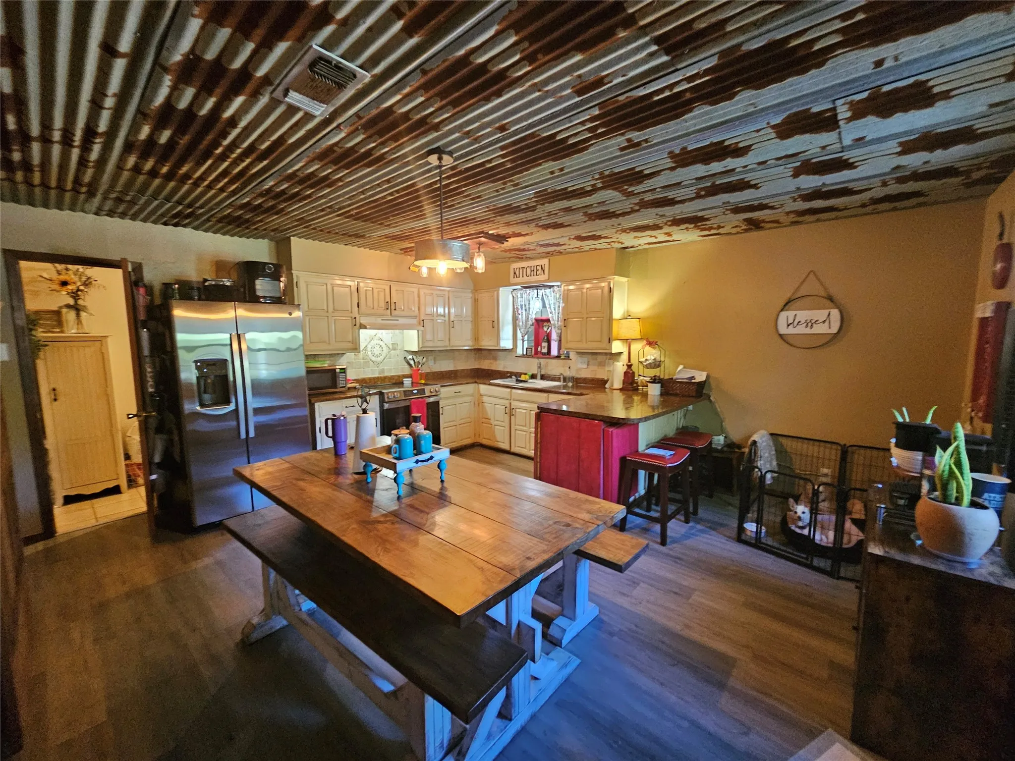 Rustic-industrial kitchen featuring a corrugated metal ceiling, wood-finish flooring, stainless steel refrigerator, white cabinetry, and a corner sink