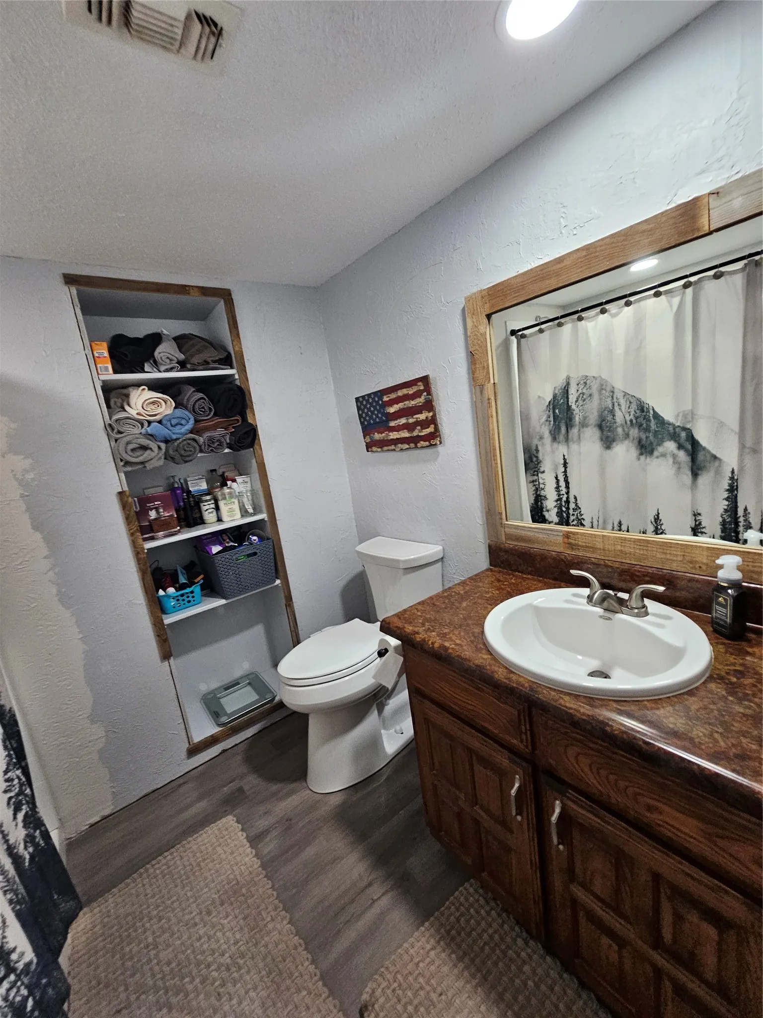 Bathroom featuring a wood-finish vanity with an integrated sink and brushed nickel faucet, a coordinating wood-framed mirror, and wood-look flooring