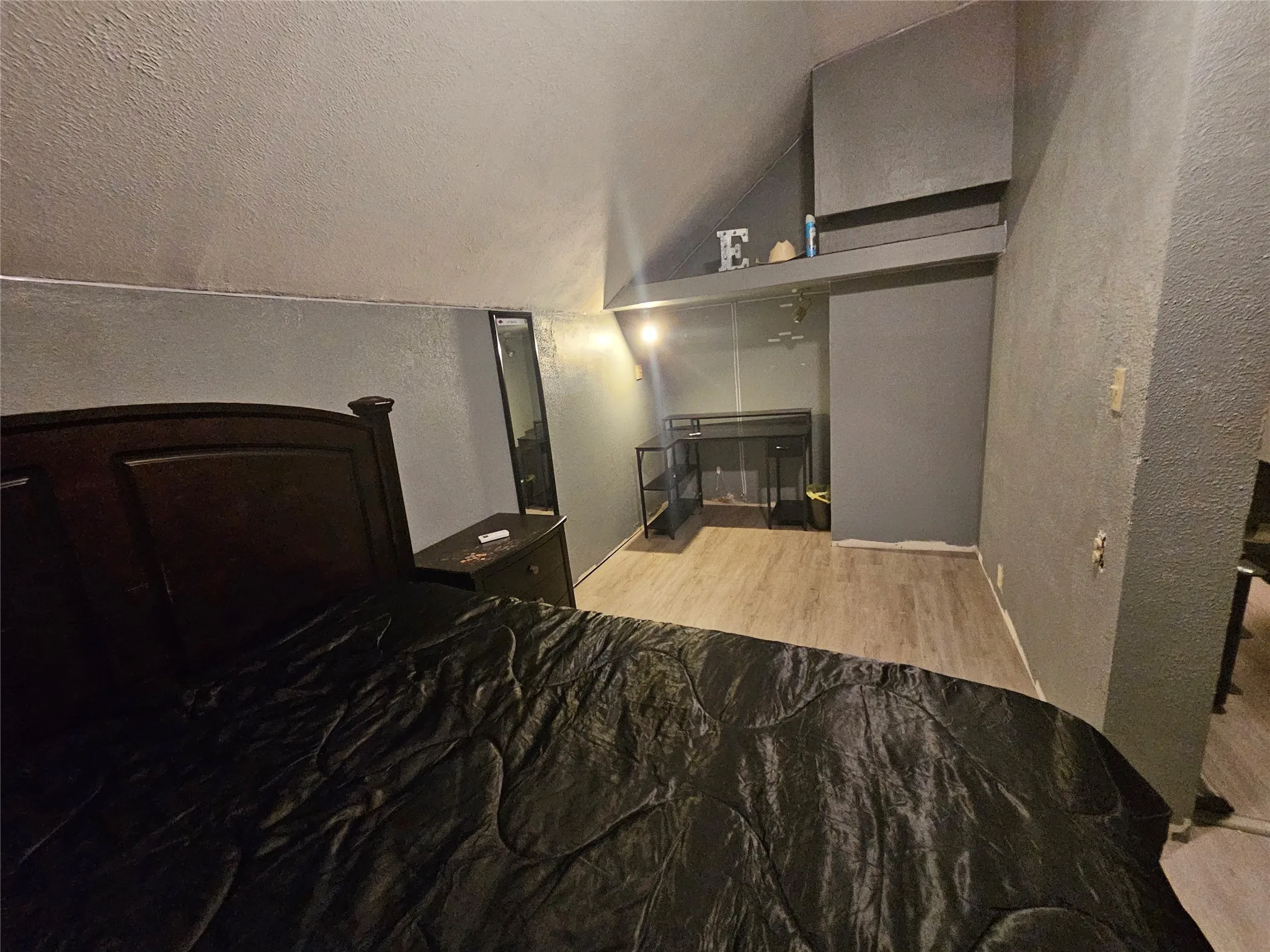 Room featuring wood-finish flooring, textured walls, and sloped ceiling