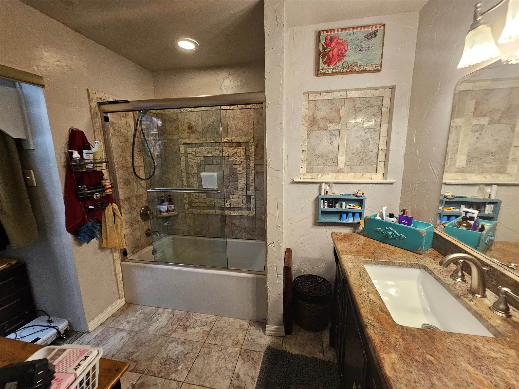 Bathroom featuring a tiled shower/tub combination with a glass enclosure, a vanity with a stone countertop and undermount sink, a large wall mirror, and tile flooring