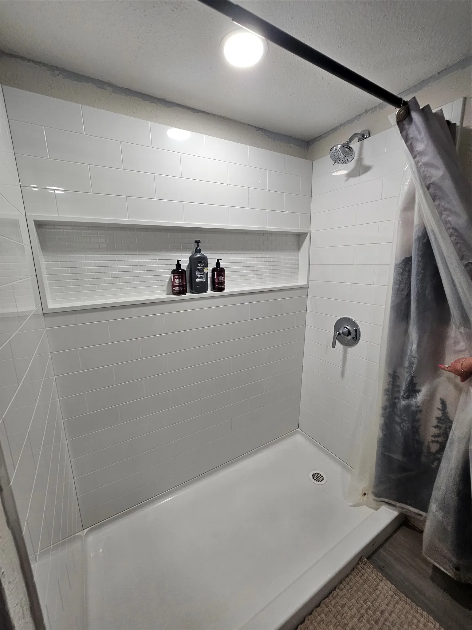 Shower enclosure featuring white subway tile, a built-in tiled niche, a chrome showerhead, a single-handle faucet, and recessed lighting