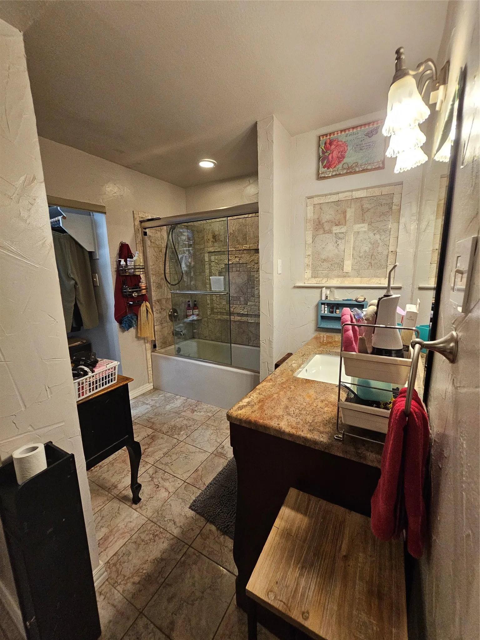 Bathroom featuring a shower-tub combination with sliding glass doors, a vanity with a surface-mounted sink, and patterned tile flooring