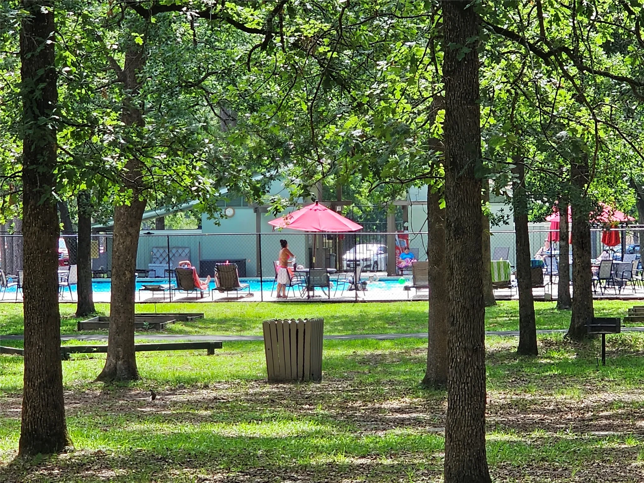 Community swimming pool with a surrounding chain-link fence, a paved pool deck, and multiple lounge chairs