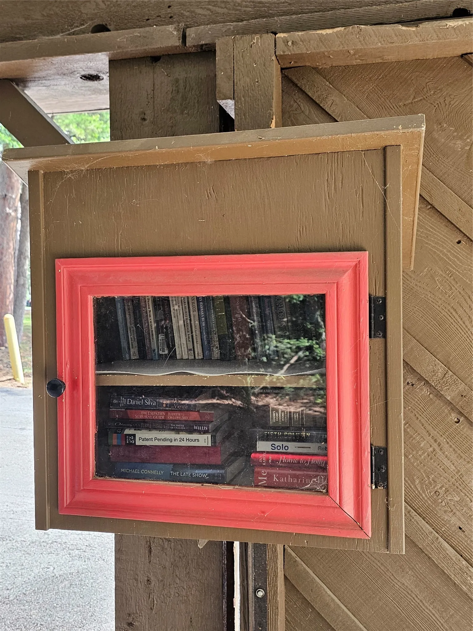 Wooden outdoor structure featuring a hinged door with a vibrant red frame and clear pane