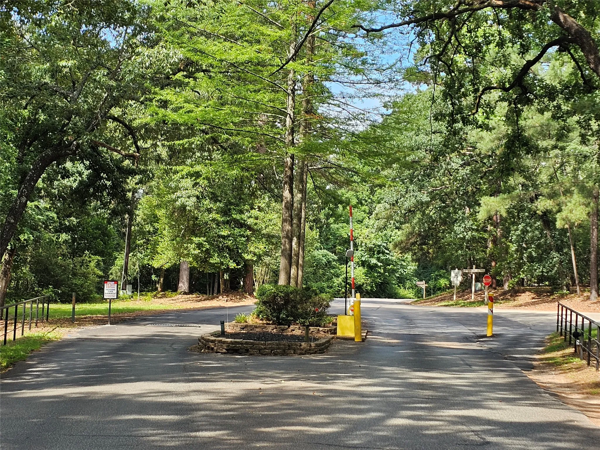 Paved entry road surrounded by mature trees, featuring a central landscaped island with stone retaining walls