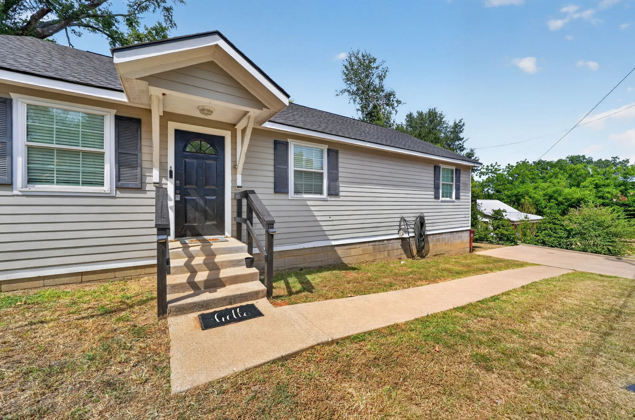 Siding exterior with a covered entryway, dark wood door, and complementing dark shutters