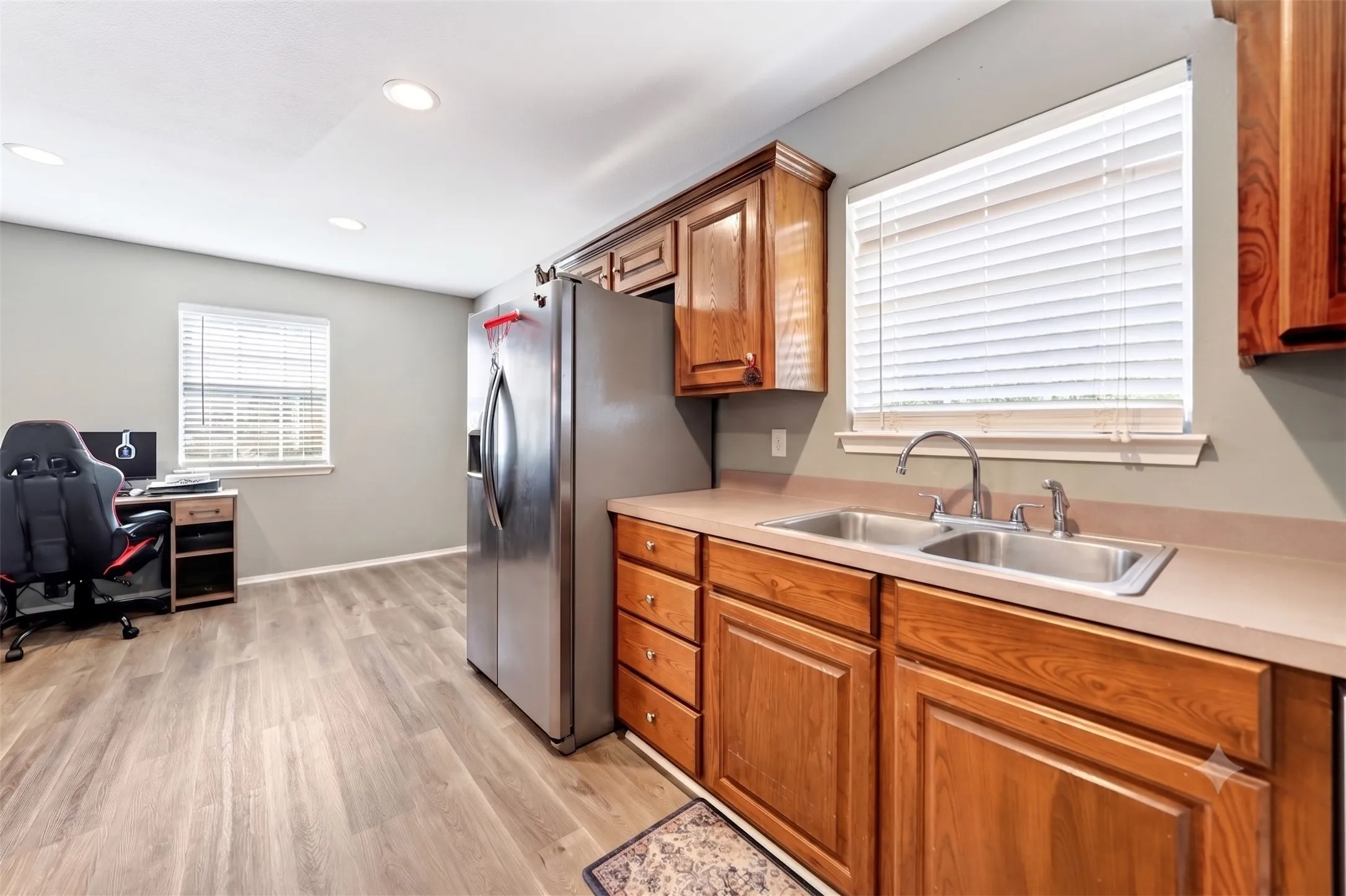 Kitchen featuring wood-finish cabinetry, a double basin stainless steel sink, and light-toned countertops