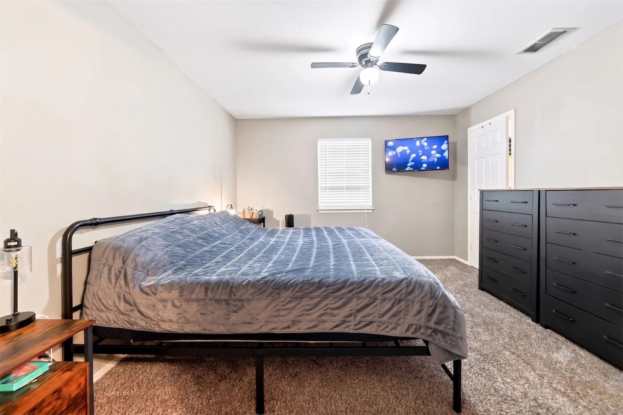 Bedroom featuring neutral wall paint, textured carpet flooring, a ceiling fan with light fixture, and a window with blinds