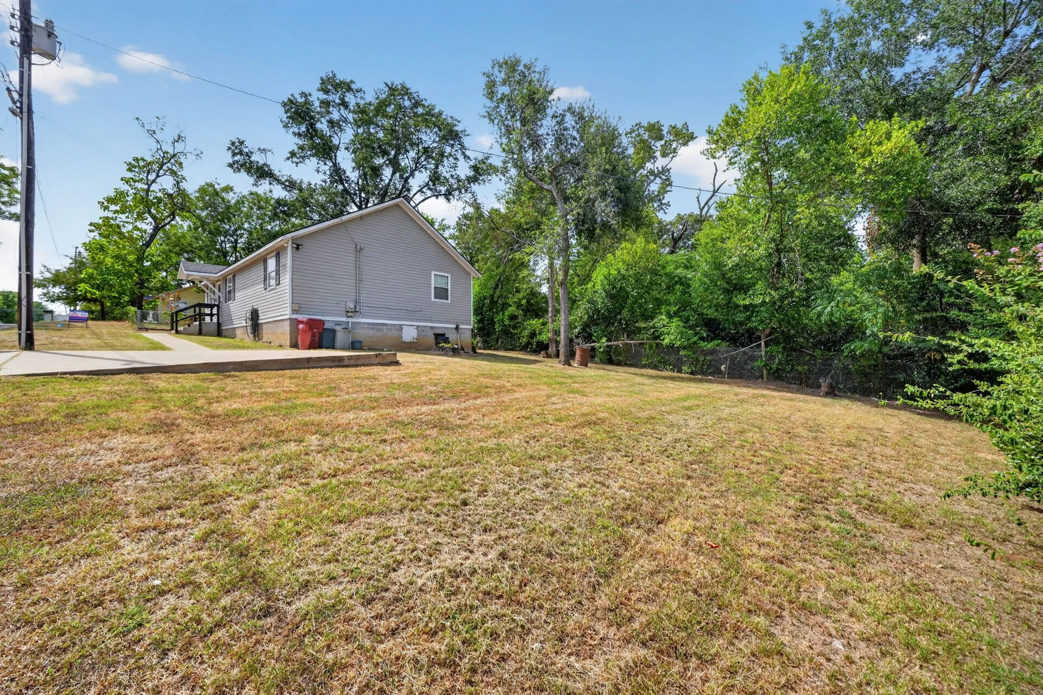 Exterior siding property with a concrete walkway, mature trees, and a chain link fence