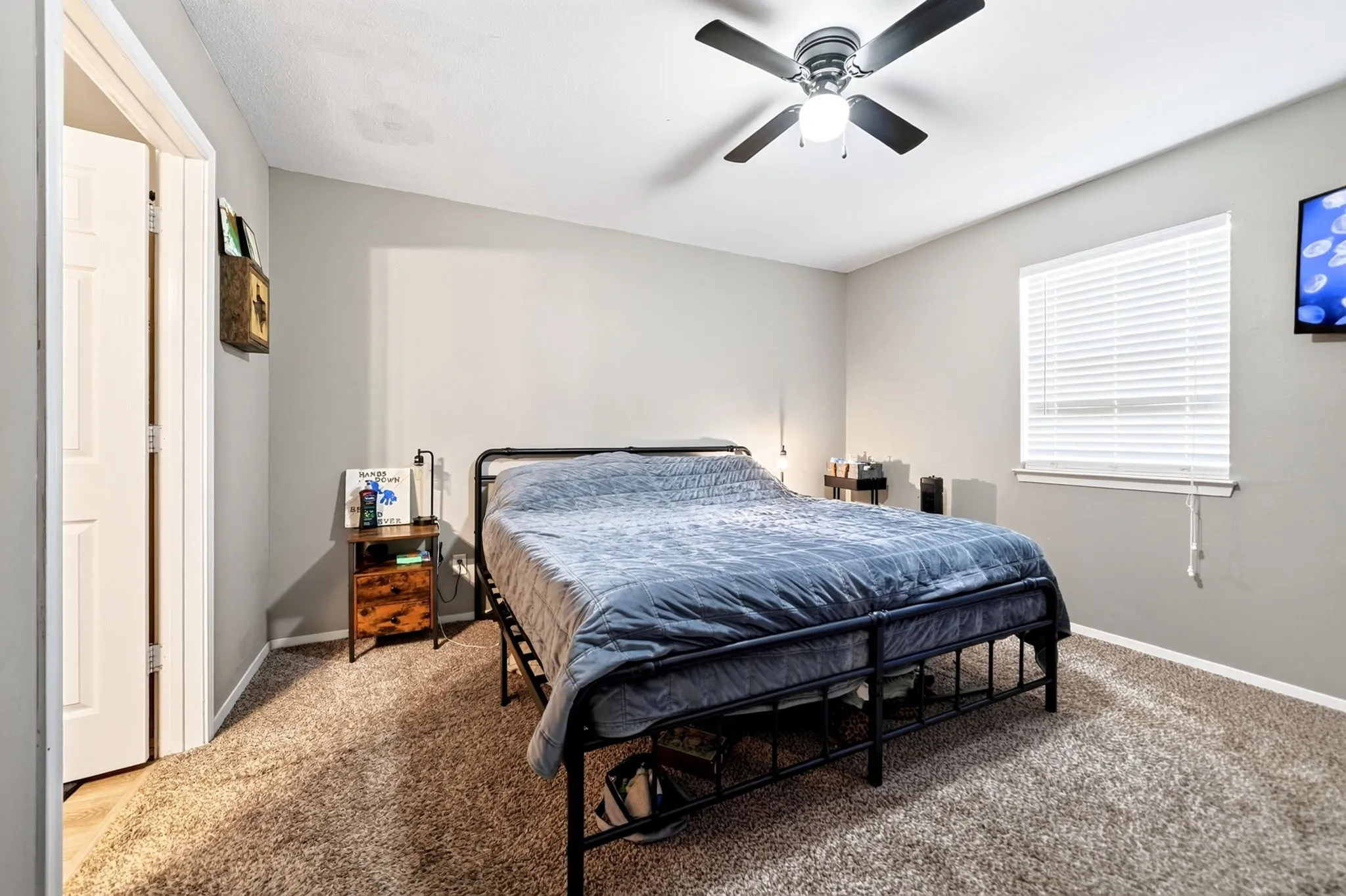Carpeted interior room featuring light gray walls, a window with horizontal blinds, and a ceiling fan with integrated lighting
